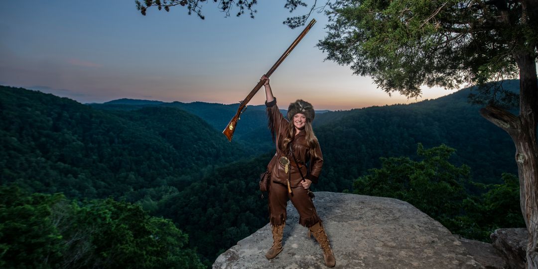 woman in buckskins holding rifle aloft
