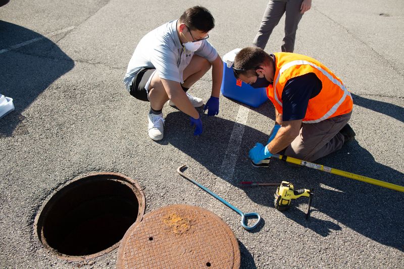 Zheng Dai (left), an epidemiology postdoctoral researcher, and Brian Lemme, an environmental health and safety specialist at WVU, prepare to collect a wastewater sample on the WVU campus. Scott Lituchy photo.jpeg