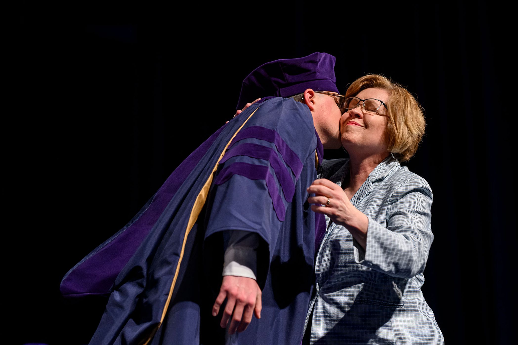 man kisses woman on cheek during graduation ceremonies
