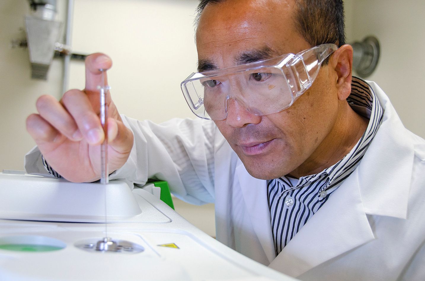 John Hu works in a laboratory wearing a lab coat and protective goggles.