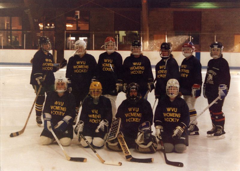 A women's ice hockey team that played for WVU unofficially in the 1990s. 11 players are posing in uniform on an ice rink with hockey sticks.