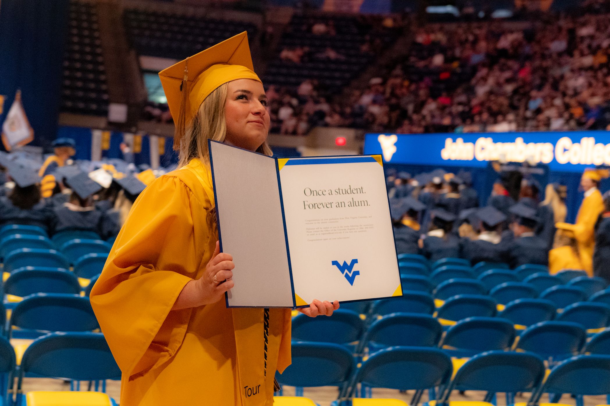 woman in gold grad regalia shows off diploma