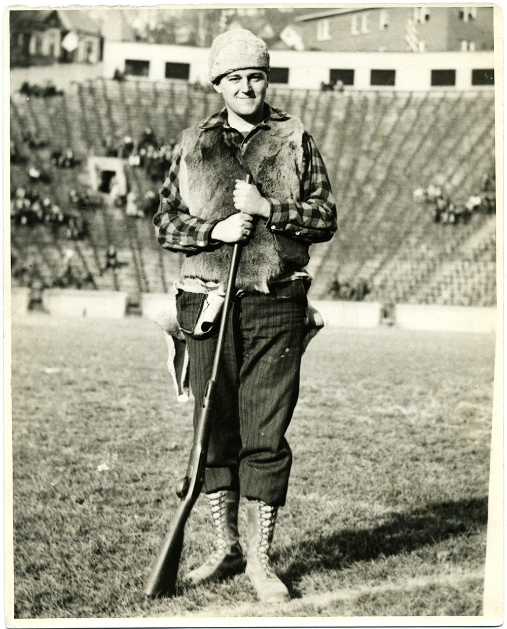 Photo of Bill Fahey, the Mountaineer in 1933, stands on Mountaineer Field with a rifle.
