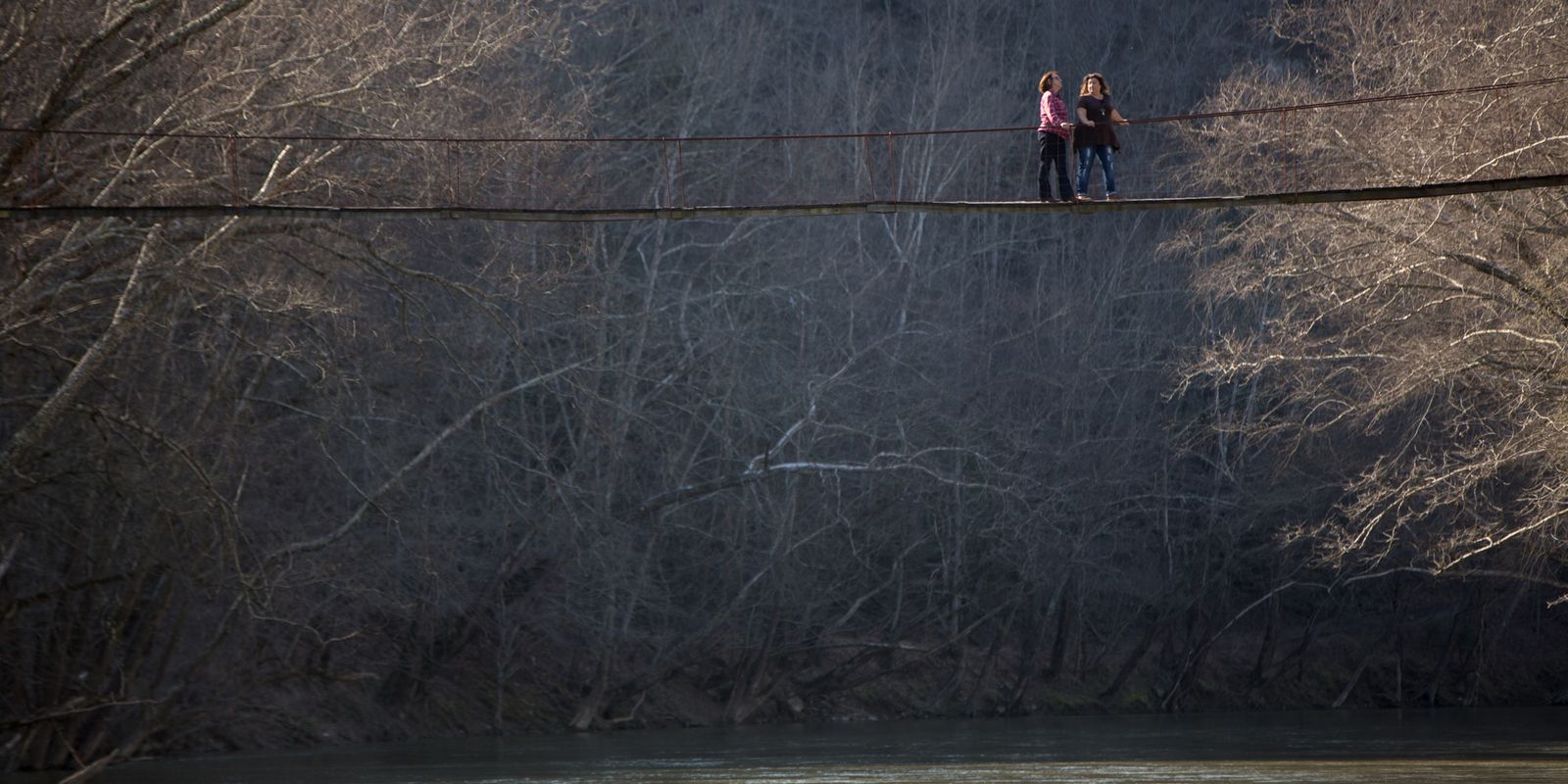 Photo of women standing on a bridge spanning a river.  The Rocky Branch Bridge crosses the South Fork of the Kentucky River and connects communities to the outside world in the event of flooding. March 9, 2017 By Nancy Andrews