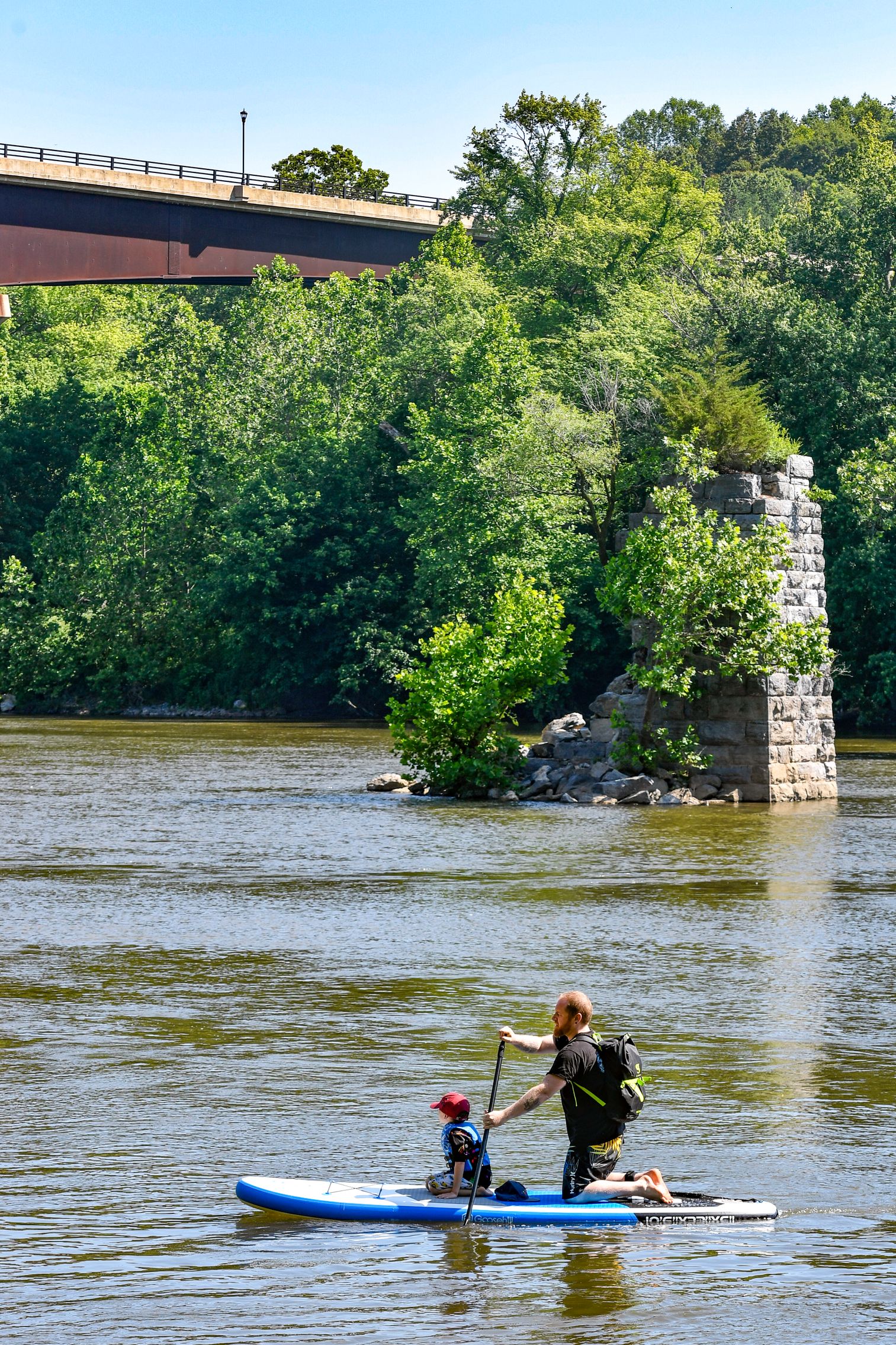 An adult and child paddle board in a river past an old brick bridge support near Shepherdstown.