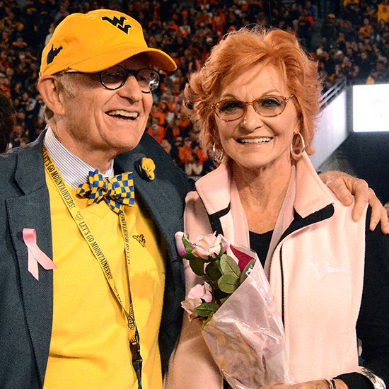 Gordon Gee with his arm around Betty Puskar, who is holding roses. They are at a football game.