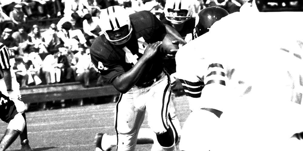 Jim Braxton on the field carrying the football while Cincinnati players run toward him.