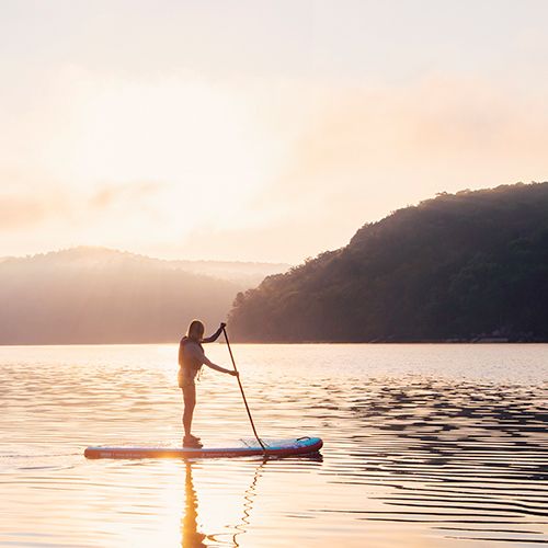 A woman stands on a paddleboard with oar at sunset on Summersville Lake.