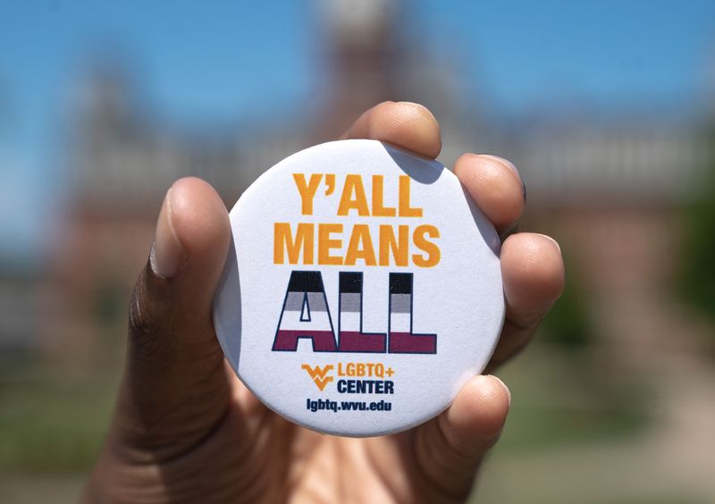 Hand holding up a button that says "Y'all means ALL.