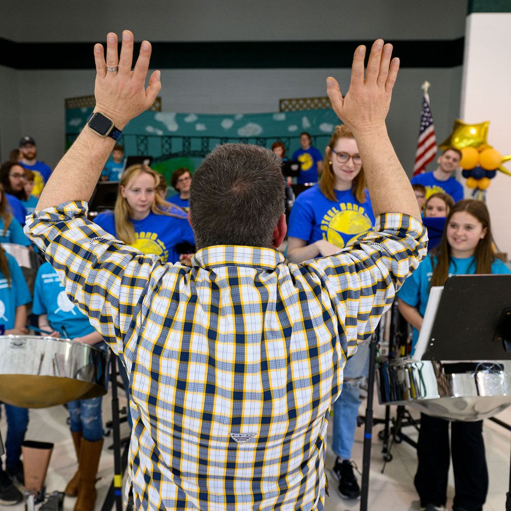 man raises hands in the air in front of steel drum musicians