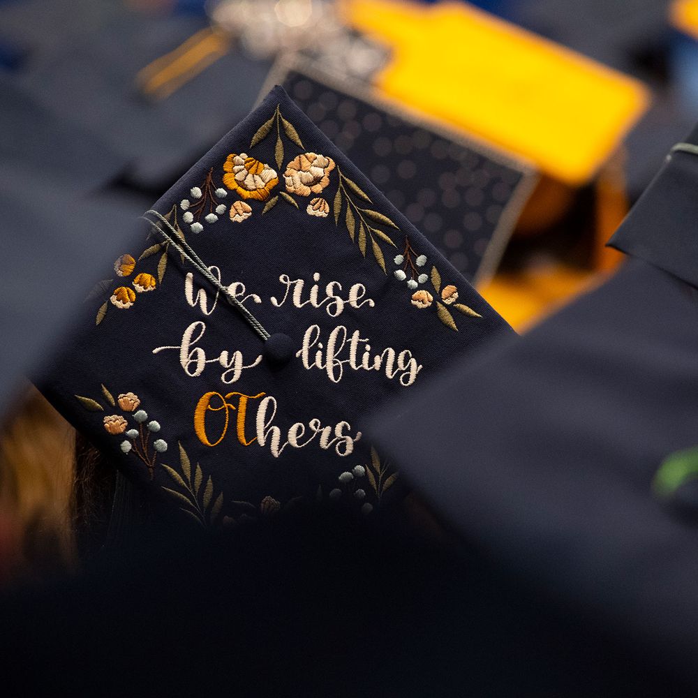 decorated mortarboard "We rise by lifting others" embroidered flowers