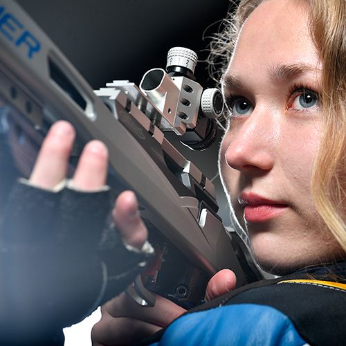 Verena Zaisberger holds a competitive rifle in her hand while looking off frame.