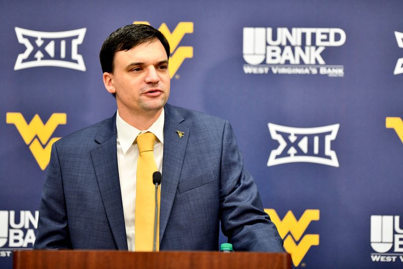 Football Coach Neal Brown stands in suit and tie at a podium for a press conference. 