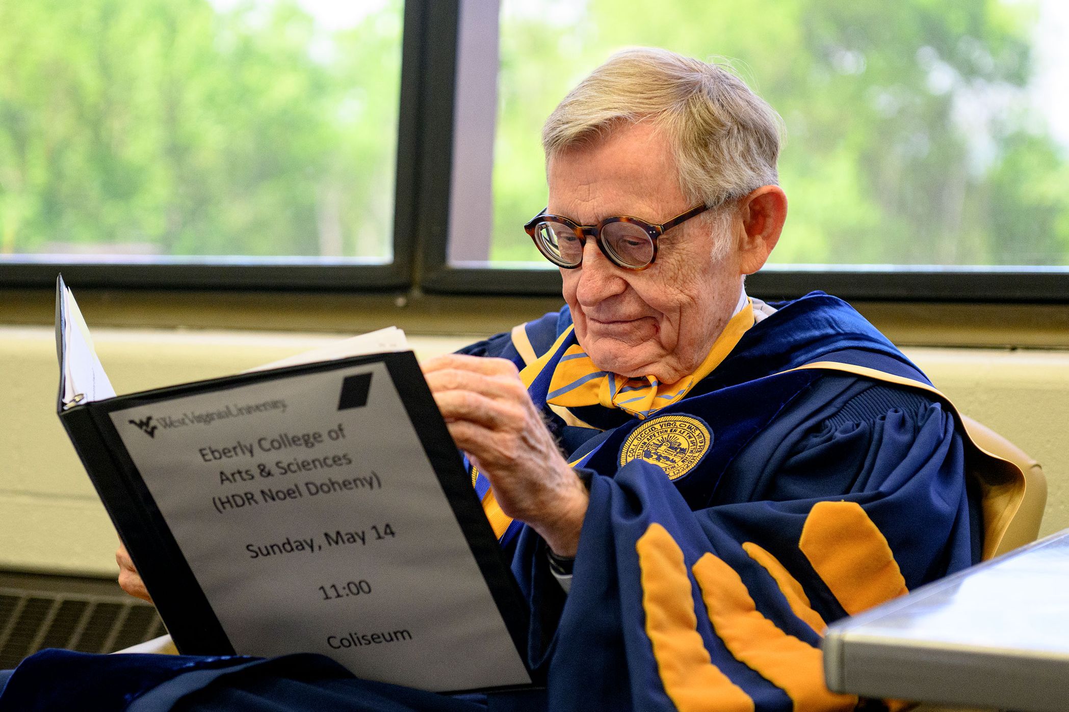man in graduation regalia reads from folder