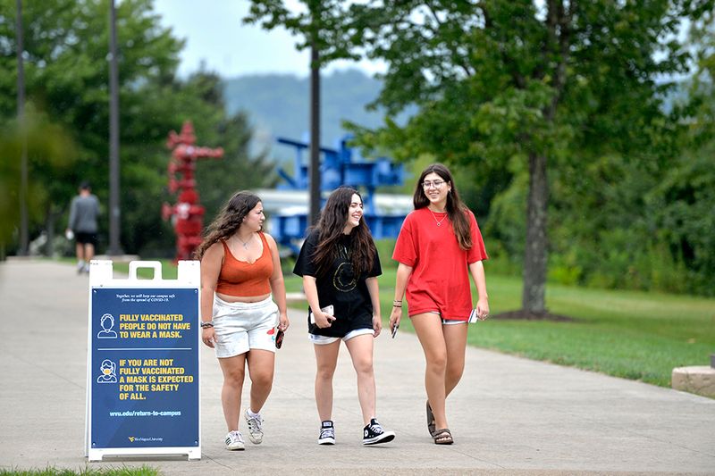 Three female honors students walk near engineering sciences building and walk past a COVID guidelines sign.