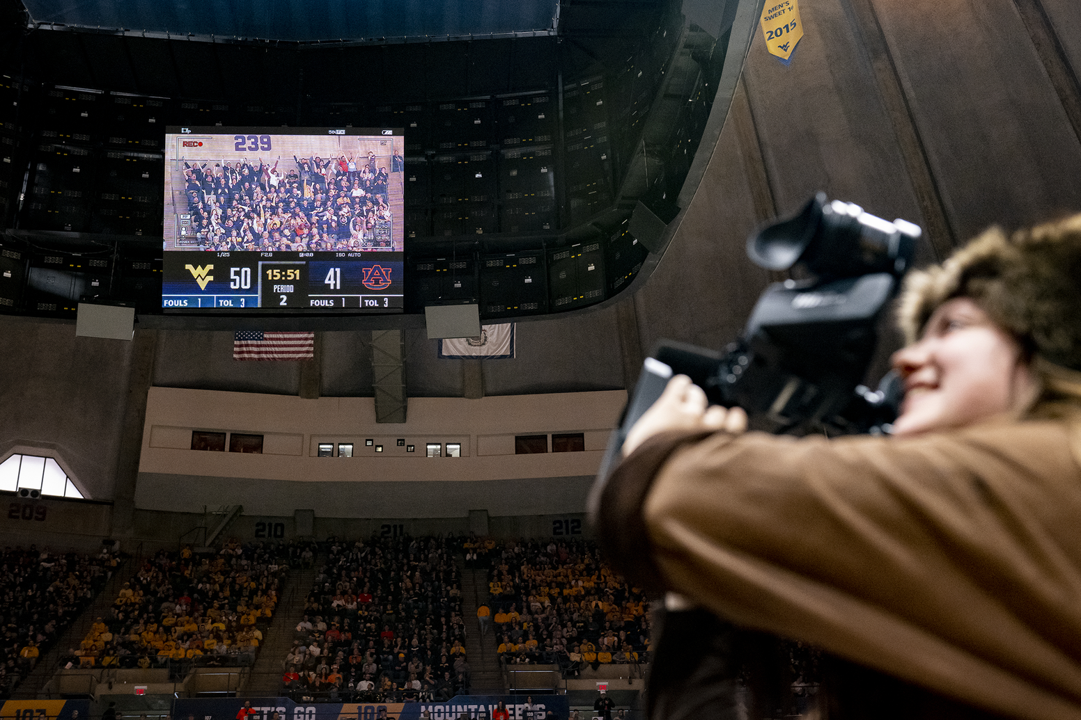 woman in buckskins holds video camera, large screen in background