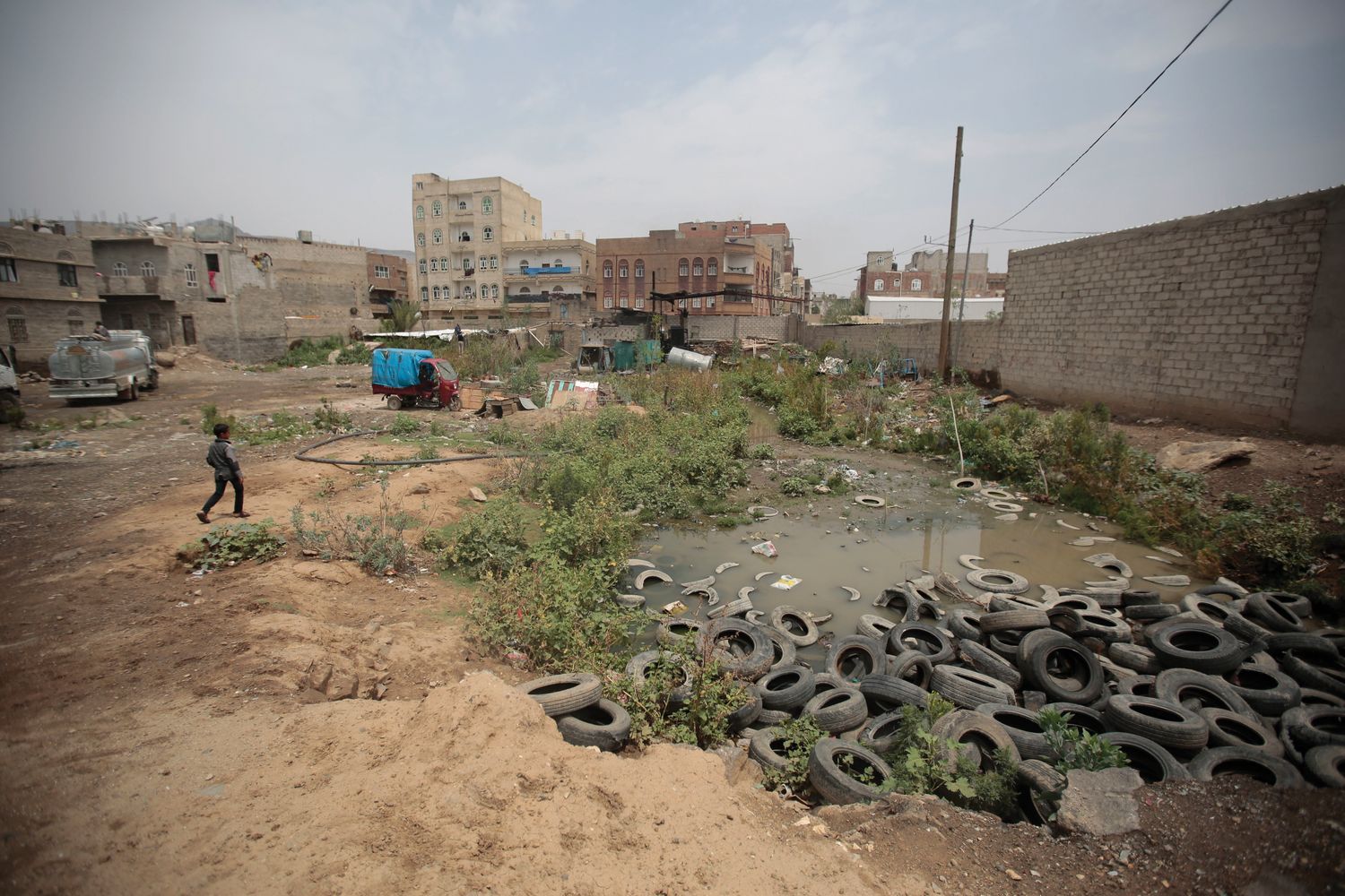 A boy walks beside a sewage swamp in Yemen.